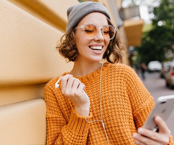 A smiling woman in an orange sweater and gray hat.